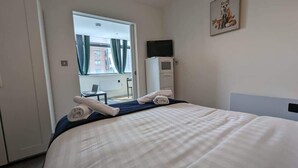 A hotel room with a bed, a desk, a chair, a television on a cabinet, and a window with curtains.