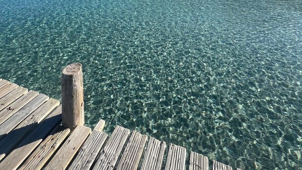 A wooden pier extending into clear turquoise water with a mountain in the background.
