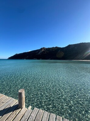 A wooden pier extending into clear turquoise water with a mountain in the background.