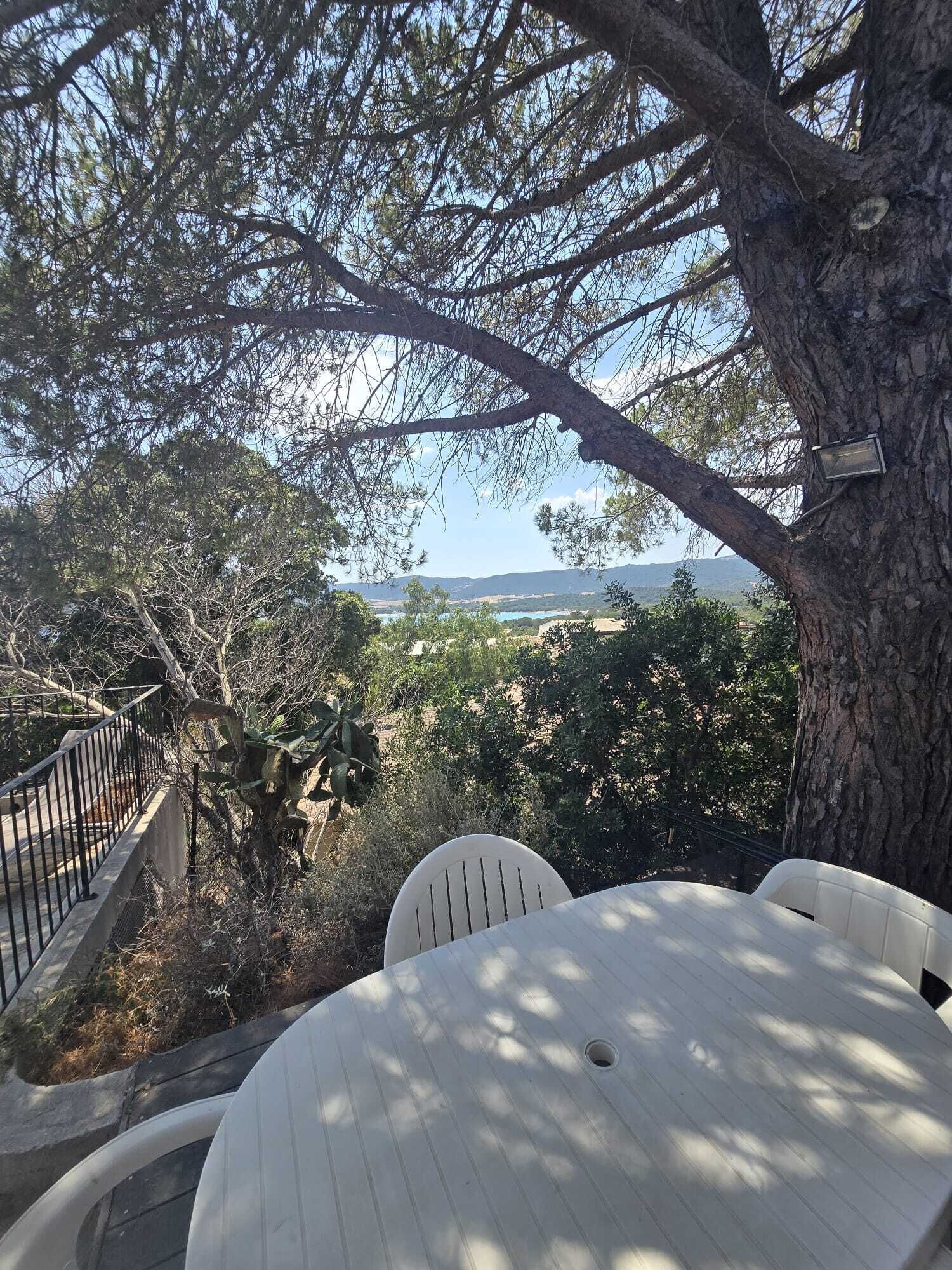 A terrace with a table and chairs, overlooking a scenic landscape with trees and a distant view of the sea.
