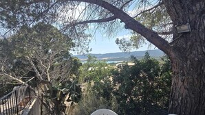 A terrace with a table and chairs, overlooking a scenic landscape with trees and a distant view of the sea.