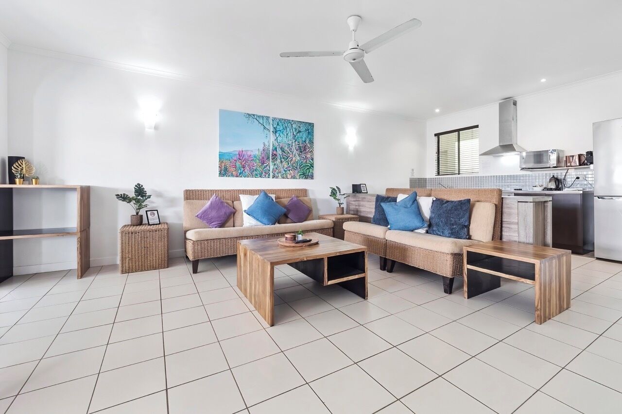A modern living room with a sofa set, a coffee table, a ceiling fan, and a kitchen area in the background.