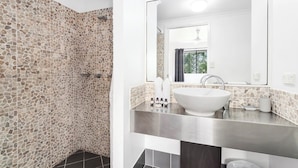 A bathroom with a stone wall, a white sink, and a large mirror. - Mango Resort Studio 45B (Palm Cove)