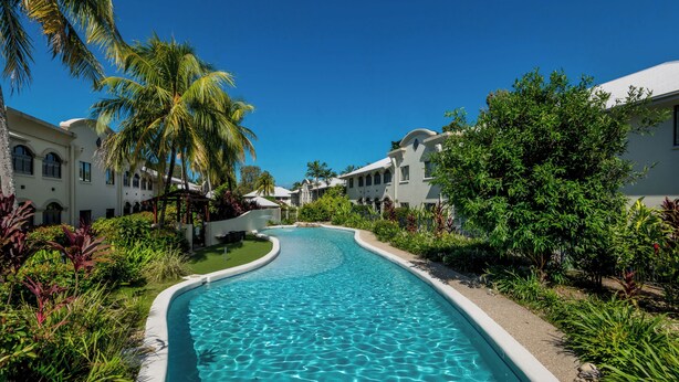 A swimming pool surrounded by lush greenery and white buildings with arched windows. - Mango Resort Studio 45B (Palm Cove)