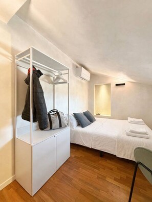 A bedroom with a bed, a wardrobe, a chair, and an air conditioning unit. - Par71 - Marco Simone golf club Roma (Marco Simone)