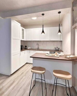 A modern kitchen with white cabinets, a wooden countertop, two stools, and pendant lighting. - Par71 - Marco Simone golf club Roma (Marco Simone)