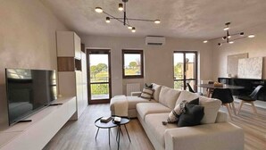 A modern living room with a flat-screen TV, a sectional sofa, a coffee table, and a dining area with chairs and a table. - Par71 - Marco Simone golf club Roma (Marco Simone)