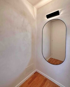 A room with a wooden floor, a white wall, and a large mirror with a black frame. - Par71 - Marco Simone golf club Roma (Marco Simone)