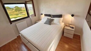 A bedroom with a bed, a nightstand, a lamp, a window with a view of a green landscape, and a radiator. - Par71 - Marco Simone golf club Roma (Marco Simone)