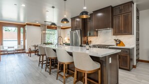 Une cuisine moderne dotée d’un îlot central, de meubles en bois foncé, d’appareils électroménagers en acier inoxydable et de luminaires suspendus.