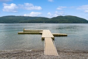 A wooden pier extending into a calm lake with a forested hill in the background. - Lake Access! Fireplace! Community Pool, Hot Tub, and Sauna! (Whitefish)