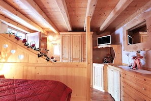 A wooden cabin interior with a bed, cabinets, a TV, and a staircase.