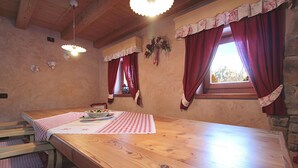 A wooden dining table with a checkered tablecloth, red curtains, and a floral wreath on the wall.