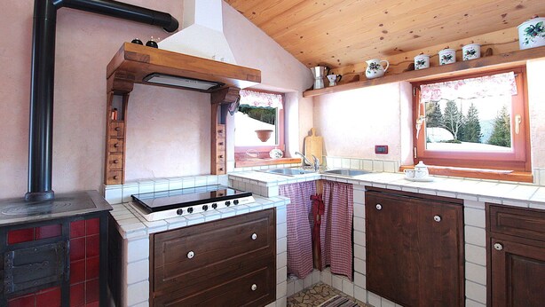 A kitchen with a stove, sink, wooden cabinets, and a window with a view of trees.