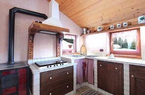 A kitchen with a stove, sink, wooden cabinets, and a window with a view of trees.