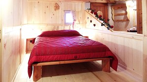 A wooden cabin bedroom with a bed, a small window, and a staircase.