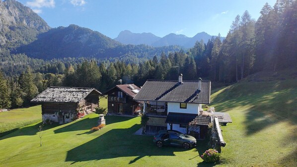 A two-story chalet with a sloped roof, surrounded by a well-maintained lawn and a mountain backdrop.
