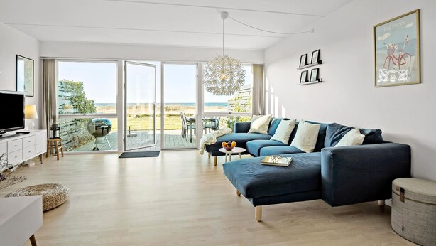 Un salon moderne avec un canapé bleu, un téléviseur et une vue sur la plage grâce à de grandes portes vitrées.