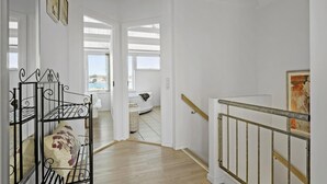 Un escalier avec une rampe en métal, un mur blanc et une vue sur une plage, visible à travers une fenêtre.
