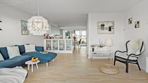 Un salon moderne avec un canapé bleu, une table ronde blanche et un fauteuil noir agrémenté d'un plaid en fourrure.
