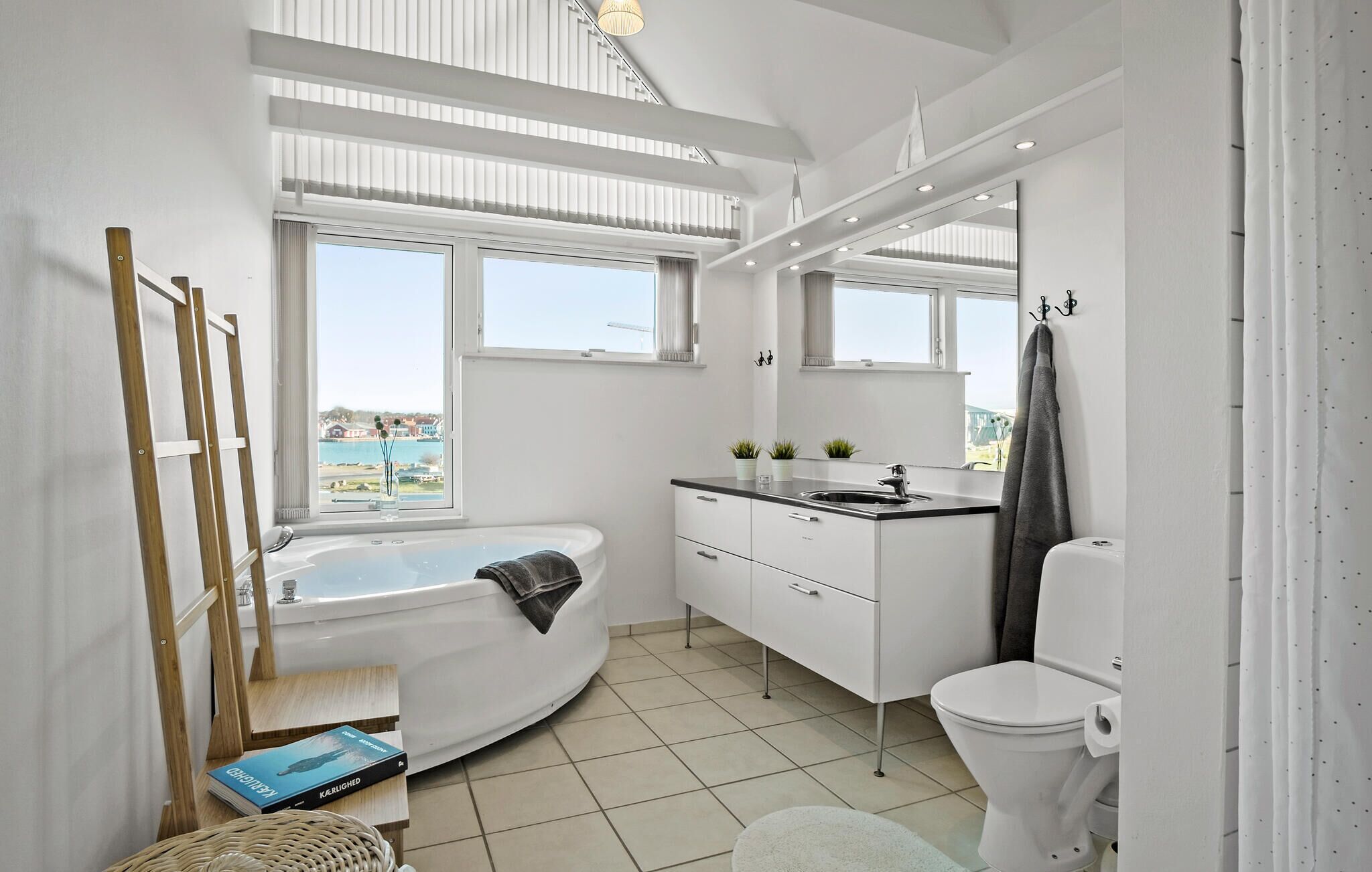 Ein modernes Badezimmer mit Badewanne, Toilette und Waschbecken. Fenster bieten einen Blick nach draußen.