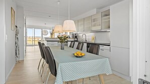 Une cuisine moderne avec des meubles blancs, une table à manger recouverte d’une nappe à motifs et un vase rempli de fleurs.
