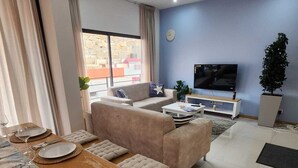Un salon moderne avec un canapé, une table basse et un téléviseur. On y trouve également un coin repas avec une table dressée pour deux personnes.