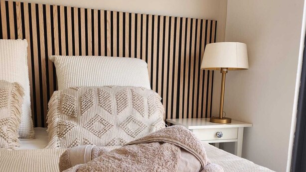 Un lit bien fait, avec une tête de lit à rayures, une lampe de chevet et une table de chevet.