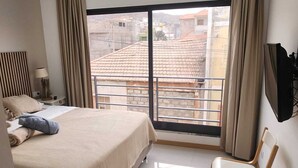 Une chambre d’hôtel avec un lit, une chaise, une télévision et un balcon avec des rideaux.