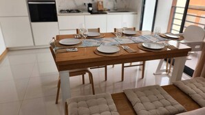 Une cuisine moderne avec des meubles blancs, une table à manger en bois dressée avec des assiettes, des verres et des couverts, et un canapé avec une structure en bois au premier plan.