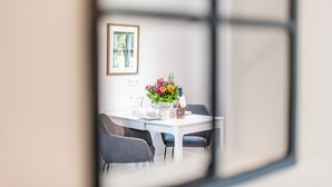A dining area with a white table, grey chairs, a vase of flowers, and a framed picture on the wall.