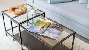 A glass-top coffee table with a magazine, a wooden bowl, and a cup of coffee on a glass table.