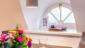 En matplats med ett bord, en vas med blommor, ett genomskinligt glas, en dekorativ tallrik med ljus och en klocka på väggen.