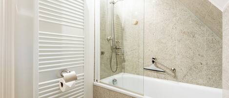 A bathroom with a glass-enclosed shower, a white bathtub, and a toilet with a paper towel holder.