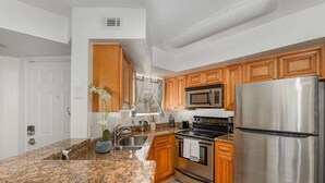 Una cocina con encimeras de granito, electrodomésticos de acero inoxidable, armarios de madera y una ventana con persianas.