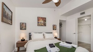 Un dormitorio ordenado con una cama, dos mesitas de noche con lámparas, un tapete verde y tres cuadros enmarcados en la pared.
