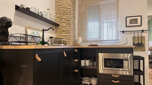 A kitchen with a built-in microwave, a coffee machine, and a stone accent wall. - Apartamento Santa Clara - Ole Solutions (Jerez de la Frontera)
