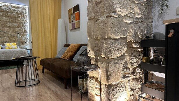 A cozy bedroom with a stone accent wall, a bed with a headboard, a bedside table, and a nightstand. - Apartamento Santa Clara - Ole Solutions (Jerez de la Frontera)