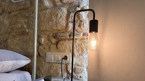 A modern room with a stone wall, a bedside table with a lamp, and a power outlet. - Apartamento Santa Clara - Ole Solutions (Jerez de la Frontera)