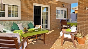 A patio area with a brick wall, a striped sofa, a glass table, and wooden chairs. - Villa Moreno - Ole Solutions (Puerto de Santa María)