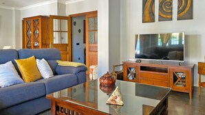 A living room with a blue sofa, wooden cabinet, and a flat-screen TV. - Villa Moreno - Ole Solutions (Puerto de Santa María)