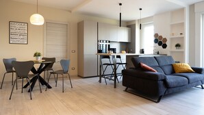 A modern living room with a sofa, dining table, and chairs. There is a kitchen area with a stove and cabinets. - Cinecitt Dreams in Rome (Rome)