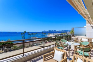 A balcony with wicker furniture, a glass table, and a view of the beach and ocean. - Croisette Gray d'Albion Penthouse, Stunning Ocean View (Cannes)