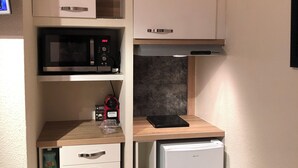 Una kitchenette compacta con microondas, un refrigerador pequeño, una encimera con hervidor y un lavamanos.