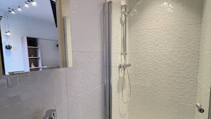 Un baño moderno con ducha envuelta en vidrio, un lavabo con espejo y pared de azulejos.
