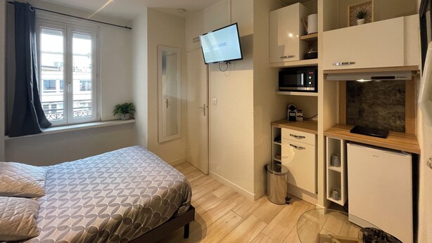 Un dormitorio moderno con cama, televisor montado en la pared y un área de kitchenette con microondas y refrigerador.