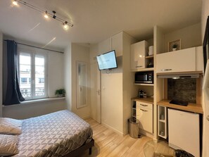 A modern bedroom with a bed, a TV mounted on the wall, and a kitchenette area with a microwave and refrigerator.