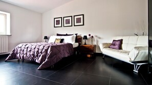 Een moderne slaapkamer met een bed, een bank en een nachtkastje. Er hangen drie ingelijste foto's aan de muur.