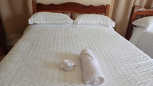 A neatly made bed with a white duvet and pillows, a rolled white towel, and a wooden headboard. - Southern Corner Motel & Restaurant (Independence and Mango Creek)