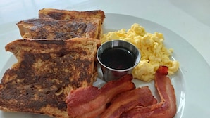 A plate with toast, scrambled eggs, bacon, and a small cup of syrup. - Southern Corner Motel & Restaurant (Independence and Mango Creek)